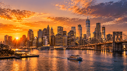 City skyline at golden hour with warm sunset light, glowing windows, river reflections, dramatic sky, and cinematic architectural photography